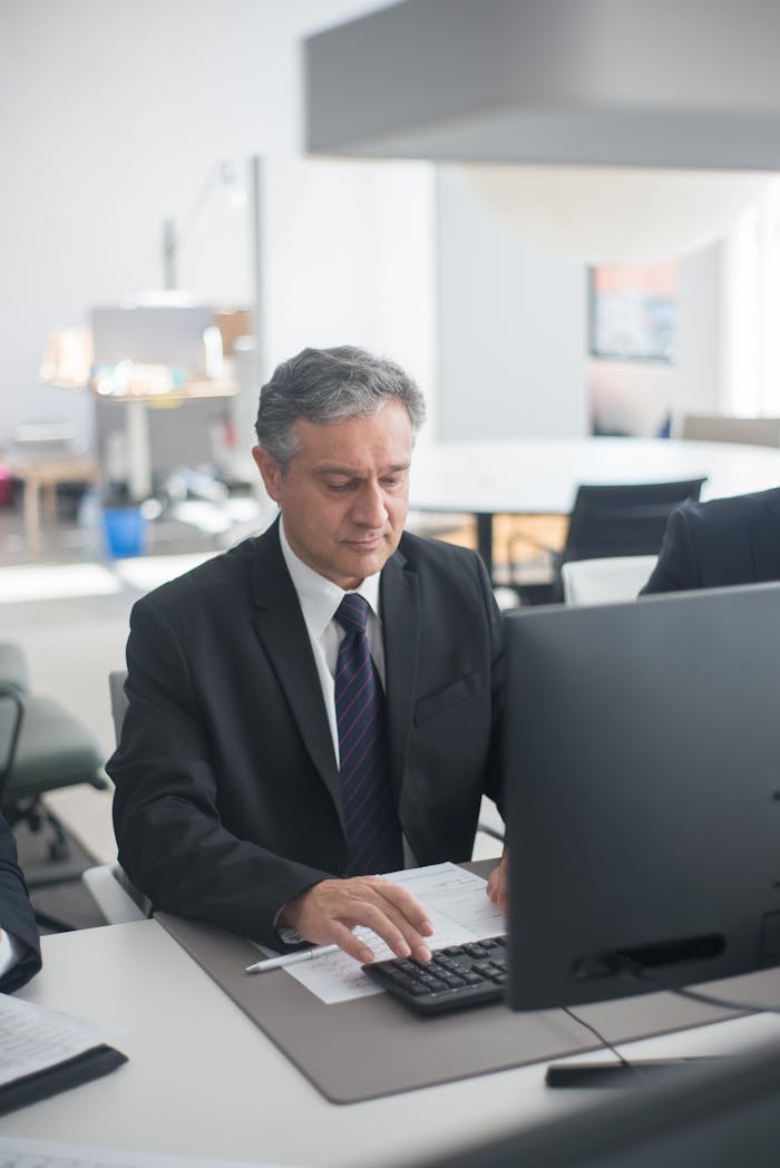 home-hero Confident businessman in a suit working on a computer in a modern office setting.